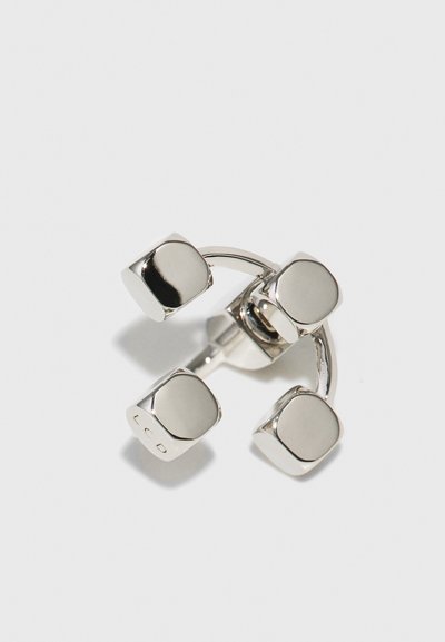 Zilveren ring met vier vierkante accenten, een gebogen band en een gepolijst oppervlak met een subtiel gegraveerd logo aan een kant.