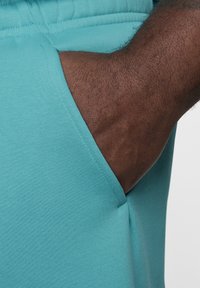 Un bolsillo de tela turquesa en unos pantalones de chándal con una mano visible insertada, mostrando la cinturilla elástica y una textura suave.