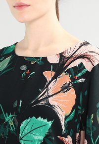 Robe en tissu noir avec un motif floral comprenant des feuilles vertes et des fleurs rose orangé, col rond et texture lisse.