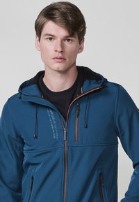 Giacca soft-shell blu con zip frontale, accenti arancioni in contrasto, cappuccio regolabile e due tasche frontali con zip.