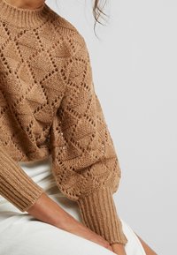 Maglione lavorato a maglia in filato marrone chiaro con un motivo a diamante testurizzato, polsini a coste e vestibilità comoda. Ideale per sovrapporre in modo informale.