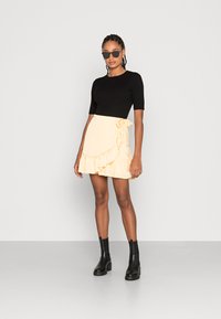 Top preto com riscas e mangas curtas, combinado com uma saia envolvente plisada amarela pálido, complementado com botins pretos e óculos de sol redondos.