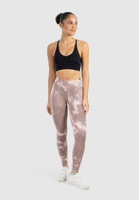 Zwarte cropped sportbeha met gerimpelde details, gecombineerd met hoogwaisted tie-dye leggings in beige en crème, afgemaakt met witte sportschoenen.