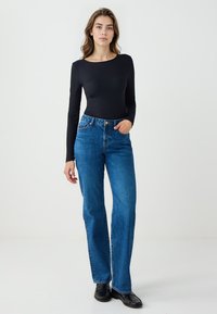 Haut noir côtelé à manches longues associé à un jean bleu taille haute à jambes droites. Le jean présente un design classique à cinq poches et une fermeture par bouton.