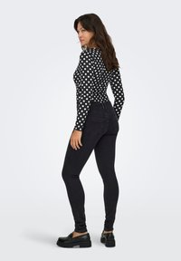 Top de manga larga negro con lunares, combinado con jeans ajustados negros de cintura alta y zapatos de plataforma negros con suela gruesa, que resaltan una silueta ajustada.