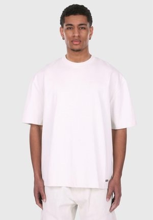 Hvit oversized t-skjorte med kort erme laget av bomull, med rund hals og en liten logomerking ved kanten. Glatt tekstur.