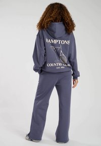 Marineblauwe hoodie en joggingset, gemaakt van zacht materiaal. De hoodie heeft een grafische print op de achterkant, met een casual pasvorm en zakken.