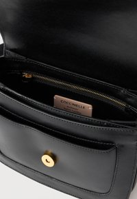 Borsa a mano in pelle nera con chiusura a scatto dorata, vano con cerniera e una targhetta con la scritta "Coccinelle Pelle Italiana Autentica".