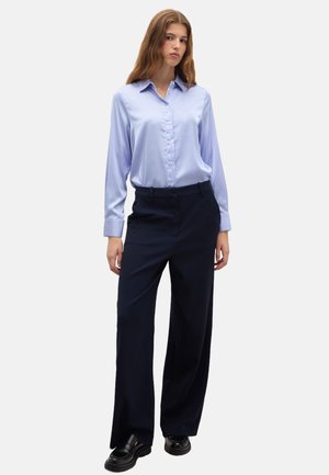 Chemise bleu clair à manches, avec col, associée à un pantalon large bleu marine et des chaussures noires. Tissu lisse et design structuré.