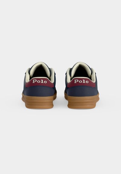 Ζευγάρι ναυτικό μπλε sneakers Polo με μπορντό ταμπάκια στη φτέρνα, λευκή επένδυση και ανοιχτό καφέ σόλες, που φαίνονται από πίσω.