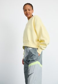 Light yellow oversized sweatshirt with a rounded neckline, paired with gray track pants featuring a green accent and Nike logo.