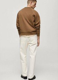 Bruine sweatshirt met raglanmouwen, gecombineerd met witte broek. Heeft een geribde onderrand en manchetten, gezien van achteren. Zwarte schoenen maken de outfit compleet.