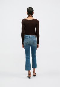 Καφέ μακρυμάνικη μπλούζα με ραβδώσεις, σε συνδυασμό με ανοιχτό μπλε καμπάνα τζιν. Το τζιν έχει ξεφτισμένο τελείωμα και πίσω τσέπες, παρουσιάζοντας ένα κλασικό casual στυλ.