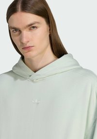 Svetlozelená mikina s kapucňou, vyrobená z jemného materiálu, s malým bielym vyšitým logom na hrudi a jemnými detailmi šitia.