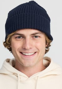 Beanie a coste navy con una texture morbida, caratterizzato da una vestibilità aderente e un bordo ripiegato, indossato sopra una felpa chiara.