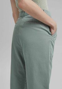 Light green, high-waisted pants made of smooth fabric with a relaxed fit. Features side pockets and subtle stitching details.