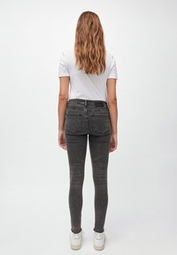 Jeans ajustados en denim gris oscuro con detalles desgastados. Combinados con una camiseta blanca y zapatillas blancas, mostrando una silueta ceñida.