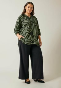 Blusa verde con motivo a righe astratte, scollatura rotonda e maniche a sbuffo corte, abbinata a pantaloni neri larghi e ballerine nere.