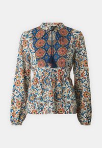 Blusa a maniche lunghe color crema, con un motivo floreale blu e arancione, vita a peplo e dettagli con frange sul collo.