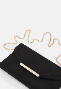 Černé semišové psaníčko se zlatým řetízkovým popruhem a elegantním zlatým pruhovým detailem. Má minimalistický design se zapínáním na klopu.