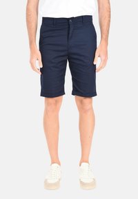 Shorts in cotone blu navy con una superficie liscia, orli risvoltati e chiusura frontale con bottone, abbinati a sneaker bianche.