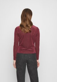 Långärmad, vinröd topp i kordmaterial med vertikala ränder och åtsittande design. Tillsammans med mörka, vida jeans. Slät textur.