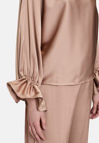 Satin-Blush-Bluse mit langen, gerafften Puffärmeln und Rüschensäumen. Glatte Textur und lockere Passform, mit geradem Saum.
