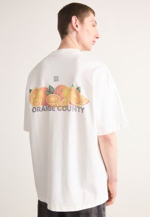 T-shirt bianco in cotone con una grafica di arance e il testo "ORANGE COUNTY" sul retro. Vestibilità ampia con scollo rotondo e maniche corte.