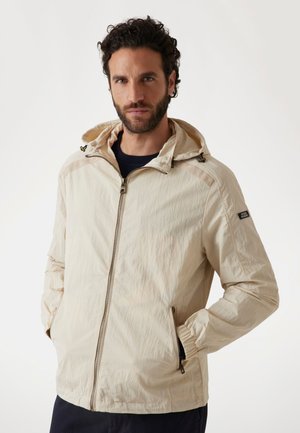 Lichtbeige jack met een capuchon, ritssluiting aan de voorkant, twee zijzakken, elastische boorden en een logo op de linker mouw. Gestructureerde stof.
