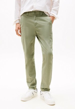 Pantalons en coton vert clair avec une coupe slim, présentant des poches avant, des passants de ceinture et une texture lisse, associés à des baskets blanches.