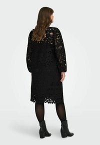 Crna čipkasta haljina s dizajnom do koljena, s cvjetnim izrezima i dugim puf rukavima. Nosi se preko crnih tajica i čizama do gležnja.