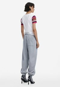 Witte t-shirt met kleurrijke gestreepte korte mouwen, gecombineerd met lichtgrijze sweatpants met een elastische tailleband en afgeknipte enkels.