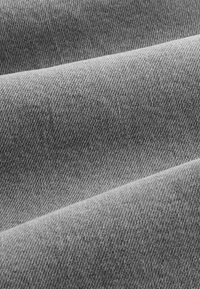 Primo piano di tessuto jeans grigio che mostra la trama a diagonale e le pieghe nella luce soffusa.