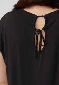 Zwarte T-shirt met een ronde hals en een keyhole-opening aan de achterkant, vastgemaakt met een zwarte trekkoord. Zacht stof met een gladde textuur.