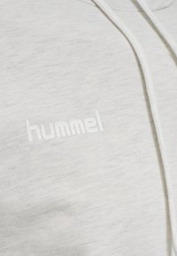 Ljusgrå hoodie tillverkad av mjukt, texturerat tyg. Har en vit logotyp "hummel" på framsidan och vita dragsnören. Slät, avslappnad design.