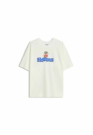 T-shirt à manches courtes blanche avec le personnage de dessin animé Shinchan au-dessus de blocs bleus épelant "Shinchan" sur le devant.
