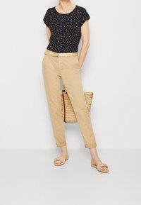 Svart blommig topp med korta ärmar, beige rull-up byxor, vävd stråväska och ljusa sandaler med flätade remmar.