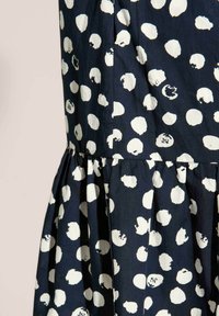 Kleid aus marineblauem Stoff mit einem gerafften Rock, der unregelmäßige weiße Punkte aufweist. Das Material scheint leicht und mit einer strukturierten Oberfläche versehen zu sein.