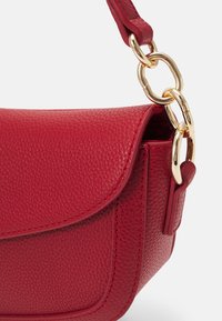 Sac à main en cuir texturé rouge avec fermeture à rabat, doté d'une sangle attachée par de grosses maillons en chaîne dorée.