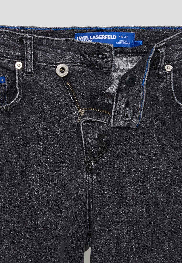 Jean en denim gris foncé avec fermeture éclair, bouton et passants de ceinture. Présente des coutures contrastées et une étiquette cousue dans la taille.