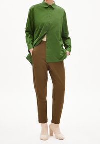 Zielona koszula z guzikami, brązowe tapered spodnie i beżowe buty na słupku. Koszula posiada kieszeń z przodu oraz długie rękawy o gładkiej fakturze.