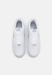 Hvide Nike Air Force 1 sneakers med glat læderoverdel, perforeret tåboks, flade hvide snørebånd og grå logo på indersålen. Sølvaccentuerede detaljer.