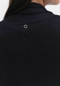 Zwarte gebreide top met een hoge kraag en een zilveren ringaccent aan de achterkant. De stof heeft een gladde textuur met subtiele stiksels.