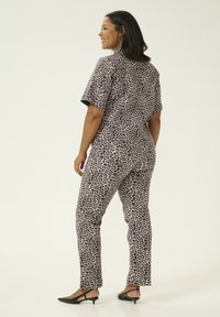 Leopardmönstrad jumpsuit med korta ärmar och åtsittande byxor, med en beige botten och svarta motiv. Bärs med svarta slingback-skor.