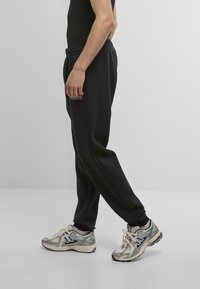 Black sweatpants with a relaxed fit, featuring an elastic waistband and a side pocket. Worn with metallic gray running shoes with blue accents.