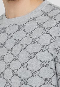 Maglione grigio chiaro con un motivo geometrico in grigio scuro, con colletto a girocollo ribattuto e una morbida texture a maglia.
