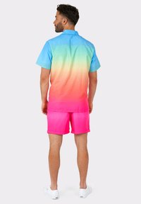 Short-sleeve button-up shirt with gradient from blue to green to pink, paired with pink shorts. White sneakers complete the outfit.