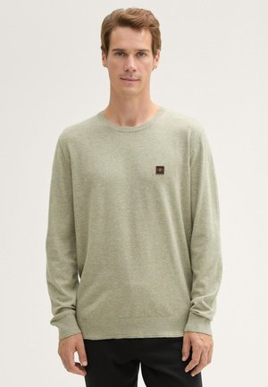 Lichtgroen shirt met lange mouwen van zacht materiaal, met een ronde halslijn en een klein zwart en oranje logo op de borst.