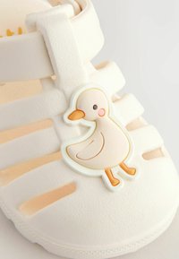 White, rubber sandal with open design, textured surface, and a duck-shaped embellishment on the side in pastel colors.