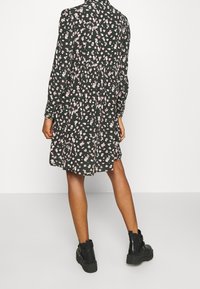 Robe noire à motifs floraux avec manches longues, taille cintrée et jupe évasée, ornée de motifs de fleurs roses et blanches. Portée avec des bottines noires.